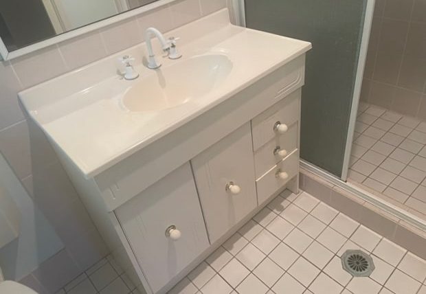 1980s style small bathroom in Sydney with pink tiles and glass shower screen with old vanity